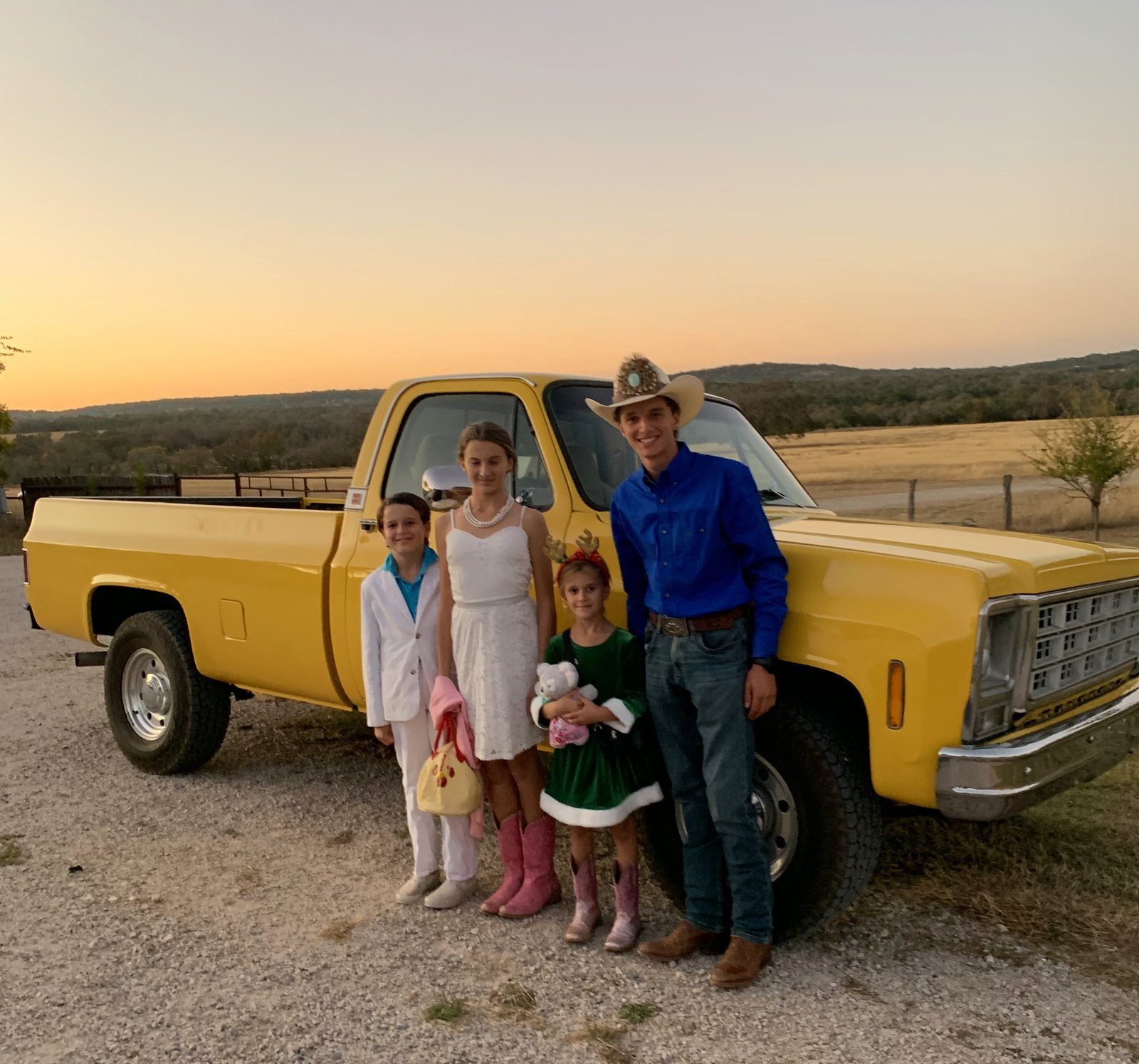 Matthew in a cowboy hat with family beside the yellow 1979 GMC at sunset