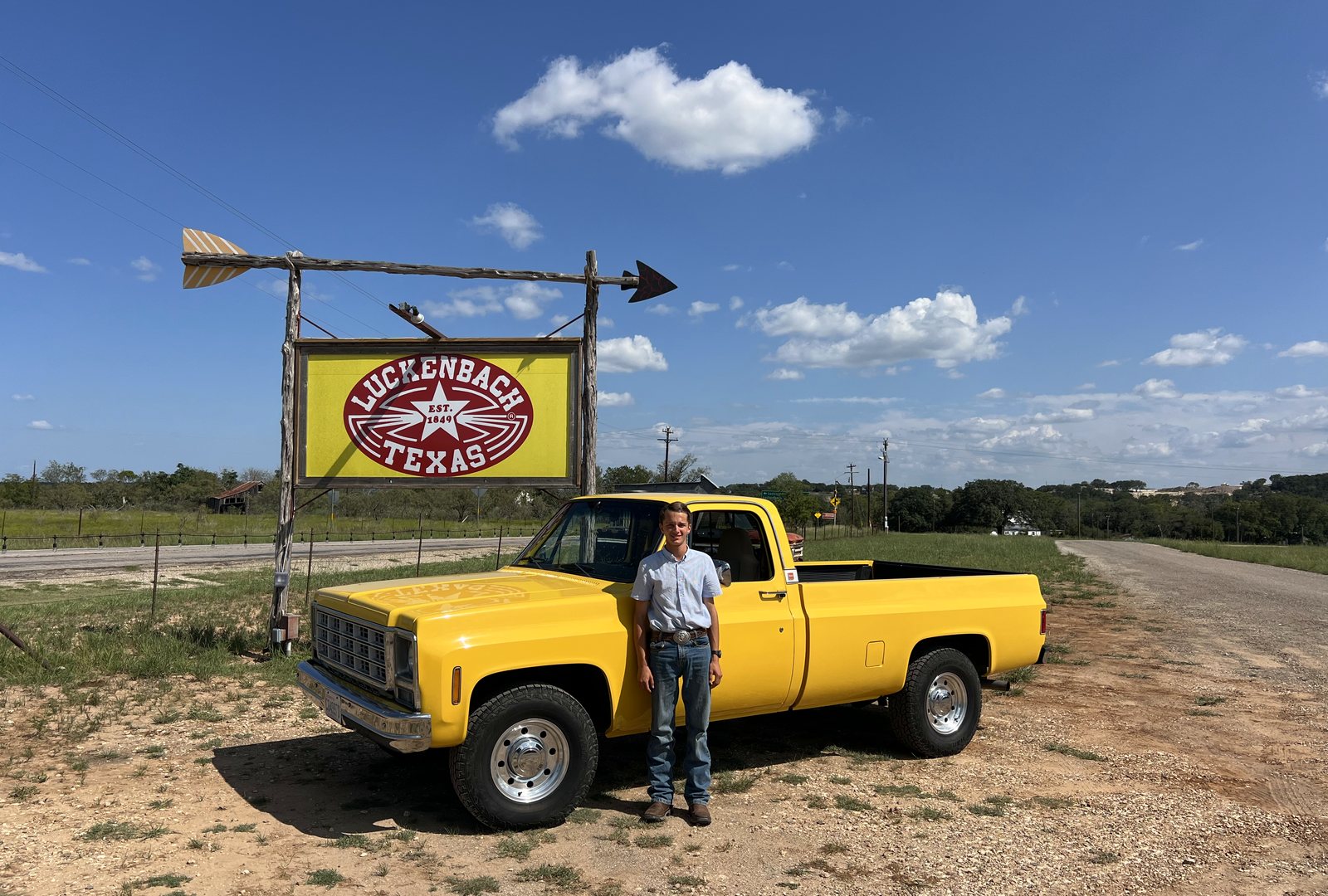 Matthew standing beside his yellow 1979 GMC pickup under the Luckenbach, Texas sign