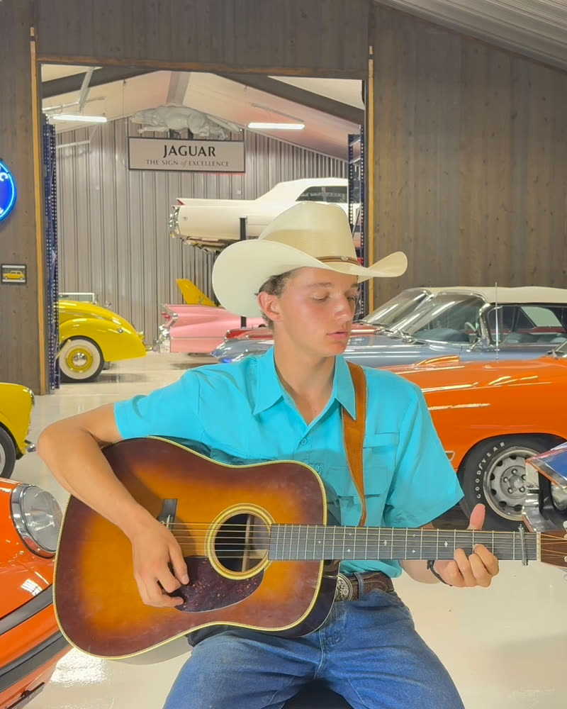 Matthew Underwood in a white cowboy hat singing and playing his sunburst acoustic guitar